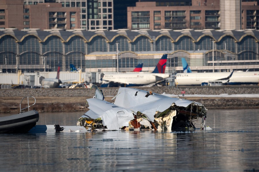 Wreckage from a small passenger aircraft floats in a river, with an airport visible in the background.