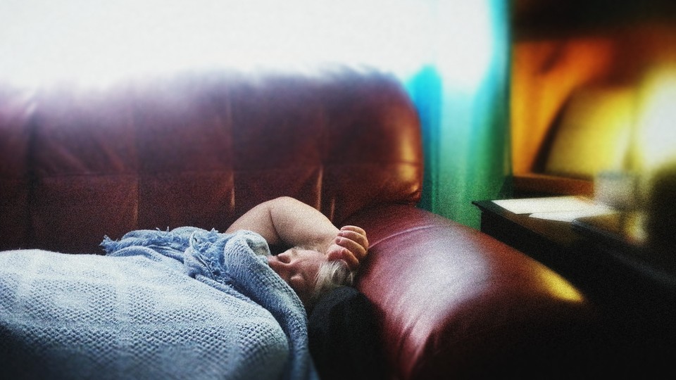 Photo of someone lying on a sofa, under a blanket, with their hand on their head