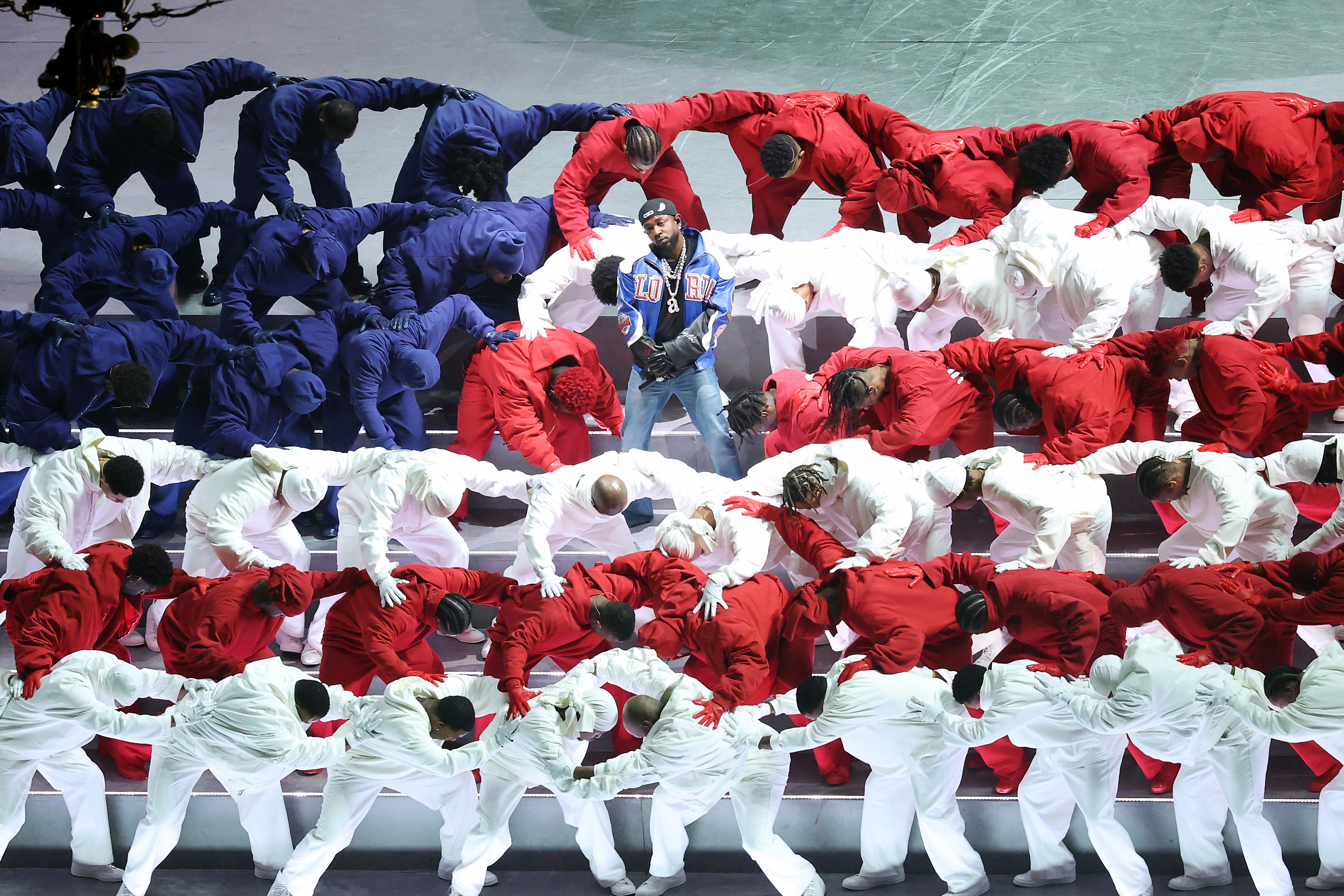 Kendrick Lamar and dancers dressed in red, white, and blue form the shape of an American flag during a performance.