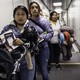 Three women, one holding a baby in her arms and pushing a stroller, stand in line awaiting to board a flight