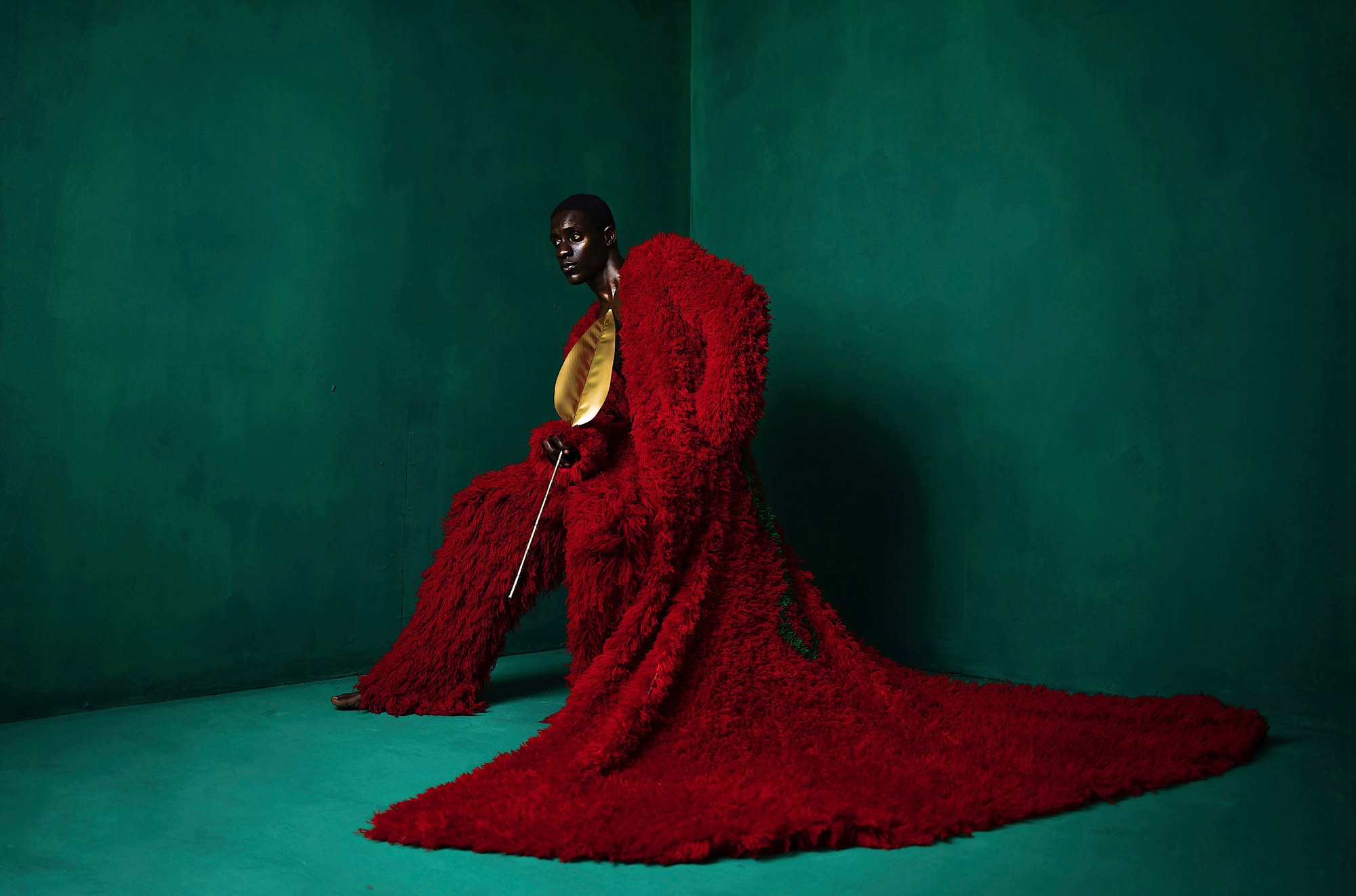 A model poses in a green room, wearing a long and flowing red garment.