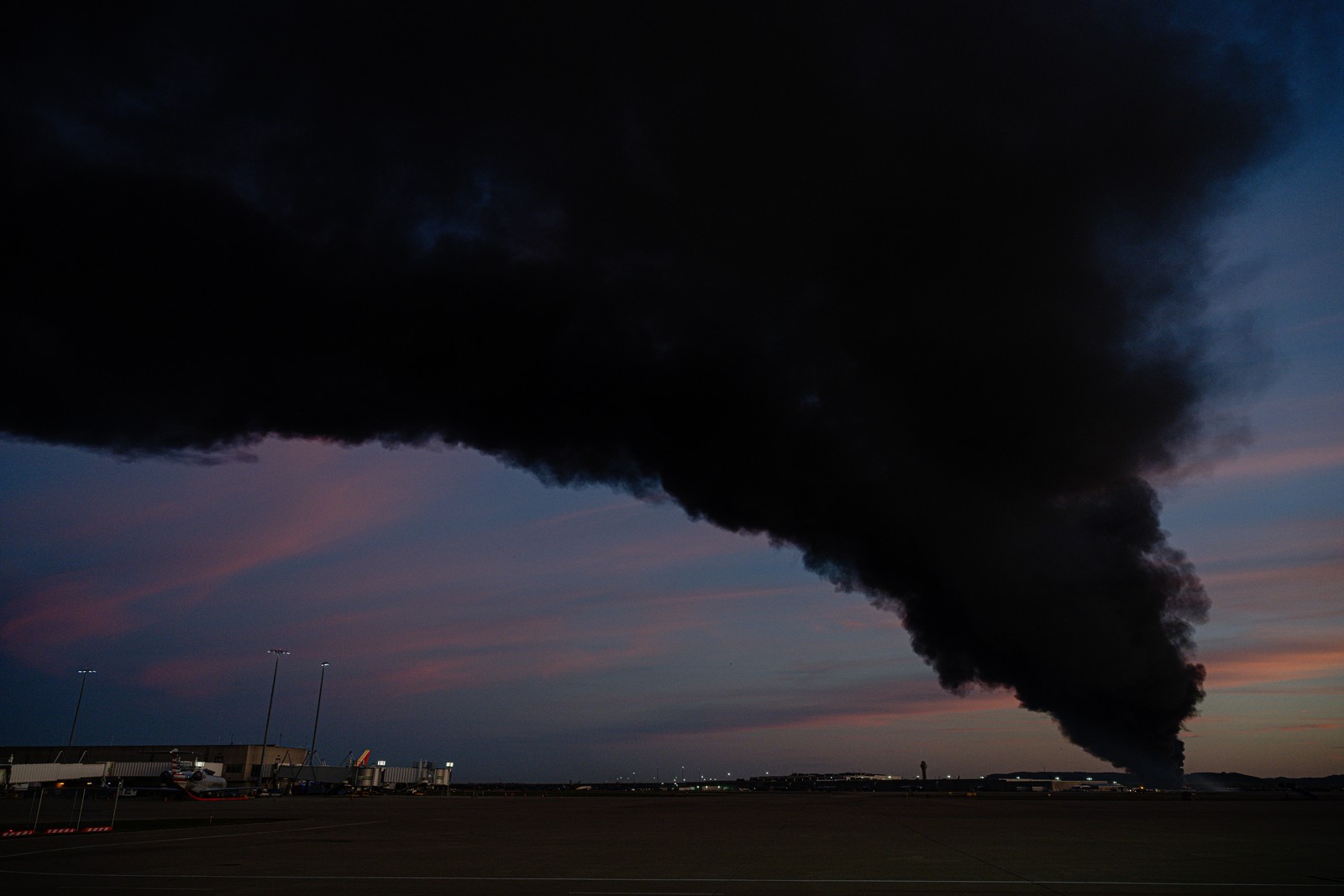 A plume of smoke rises over airport property after a plane crash.