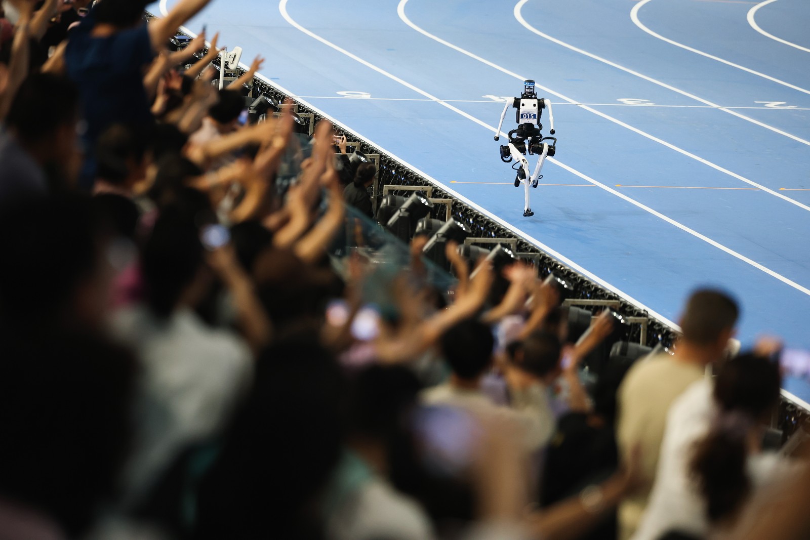A crowd cheers as a humanoid robot runs past them on a track.