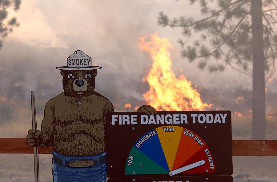 Fire burns behind a Smokey the Bear fire warning sign with its arrow pointing toward "extreme" fire danger today.