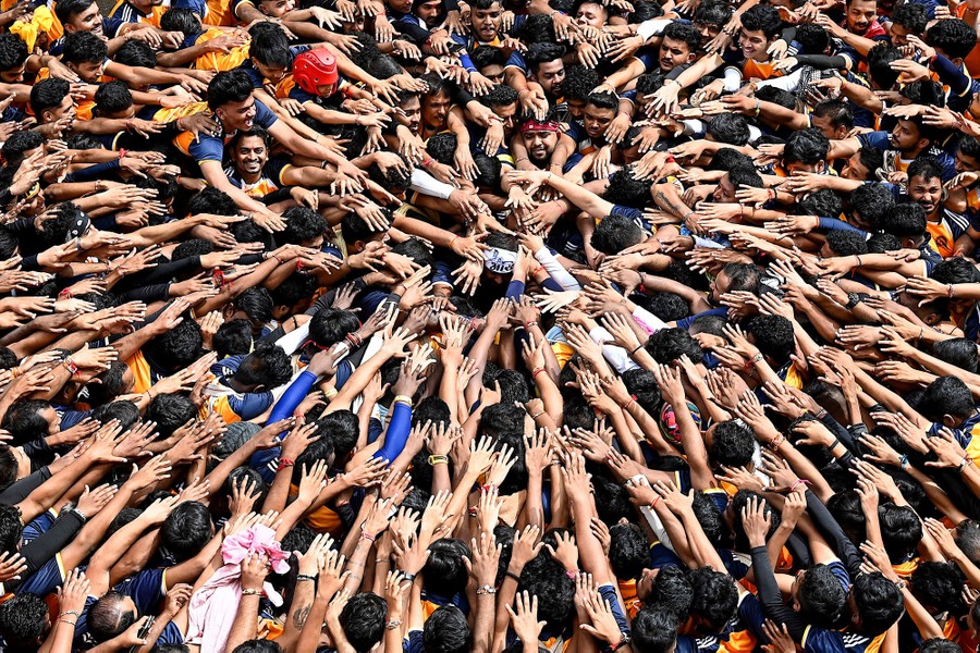 A large group of people crowd together, stretching their arms toward a point in the middle.