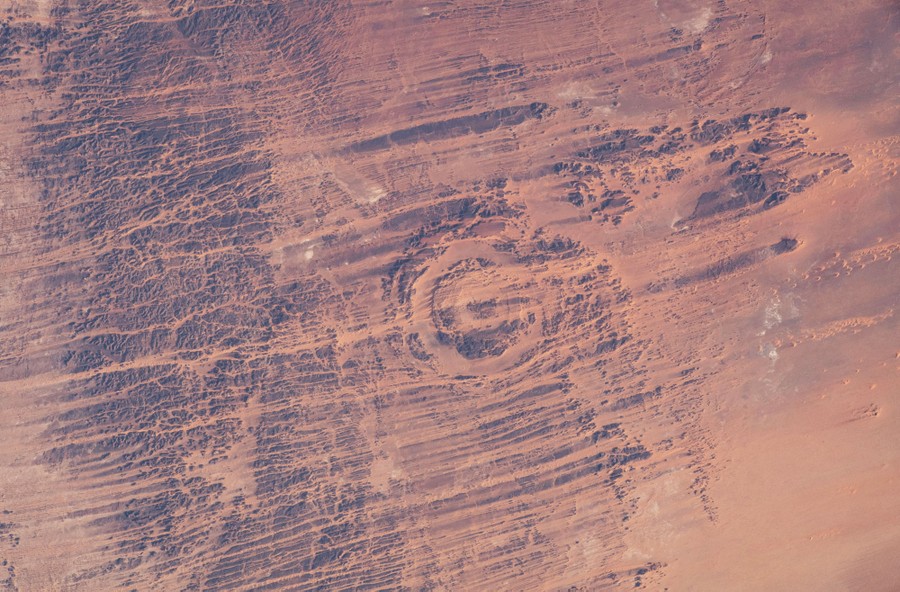 An aerial view of a long-eroded meteorite impact crater in a desert.
