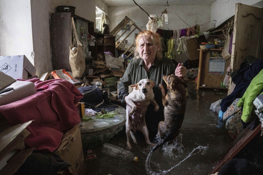 A woman holds up two small dogs inside a room in a flooded house, with water above her knees.