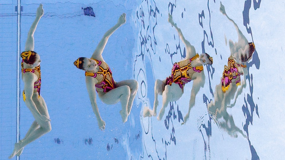 Two Japanese artistic swimmers wearing pink-and-orange suits compete at the Tokyo Olympics.