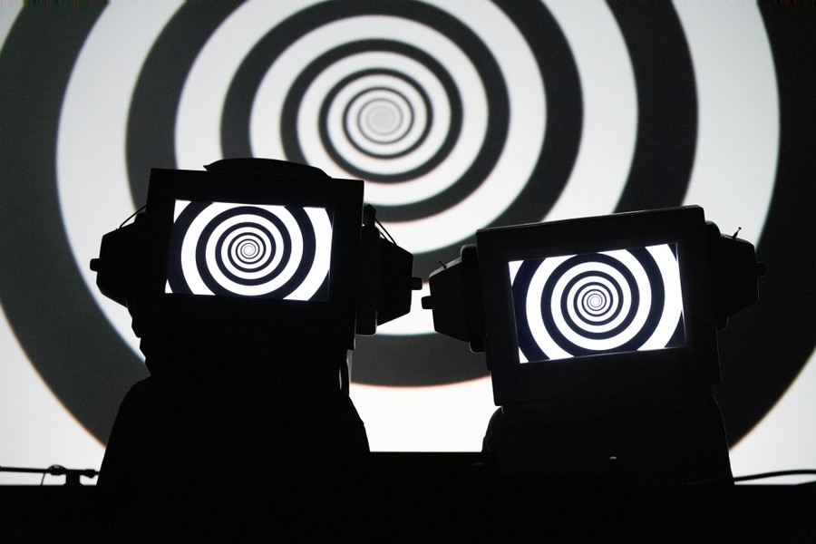 Two performers wear helmets shaped like televisions, with spiral designs on their screens.
