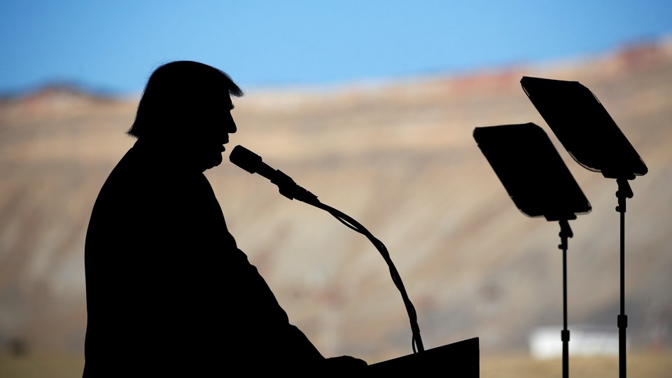 Donald Trump stands silhouetted against mountains in the background.