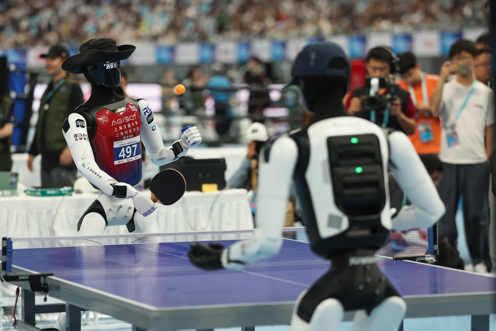 Two humanoid robots wearing hats play table tennis.