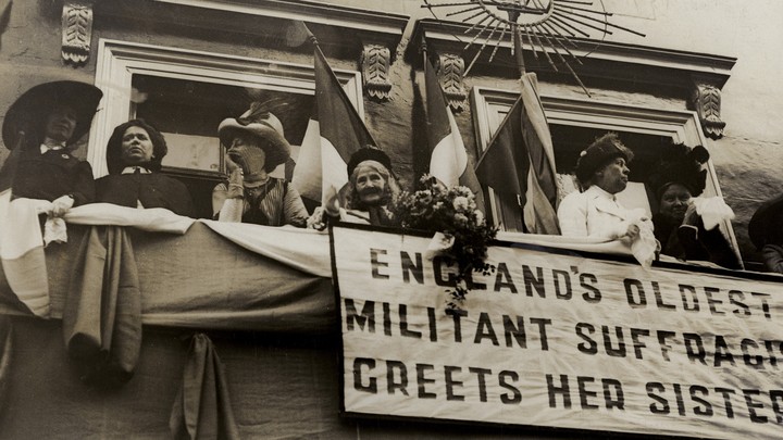 Elizabeth Wolstenholme Elmy by a banner that reads "England's Oldest Militant Suffragist Greets Her Sisters"