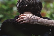 a hand wearing an engagement ring pats the back of an older woman