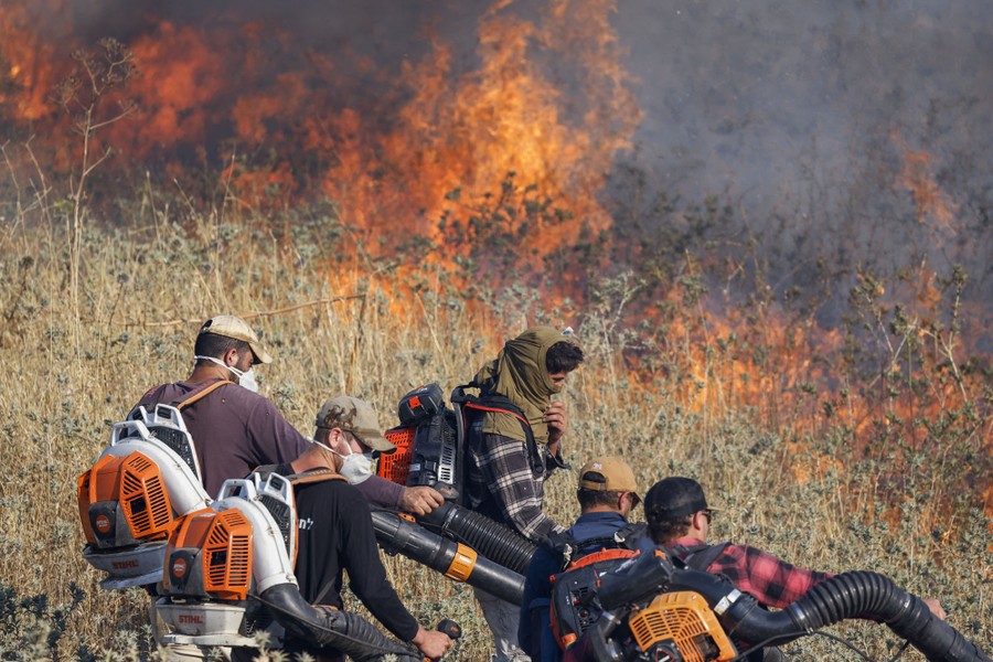 Firefighters work with leaf blowers beside a brush fire.