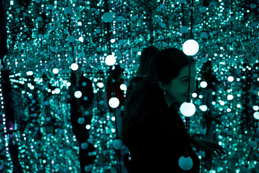 People walk through a room filled with small decorative lights and mirrored walls.