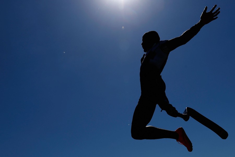 A paralympic athlete is seen in mid-air during a long jump attempt.