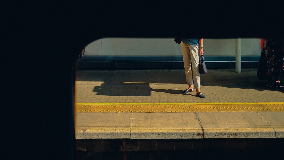 Color photograph of a woman, half in shadow, standing on a train platform.