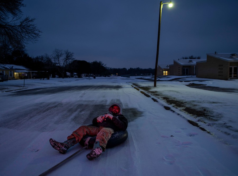 A man leans back, enjoying a beer, while sitting on an innertube that is being towed down a street by a truck at night .