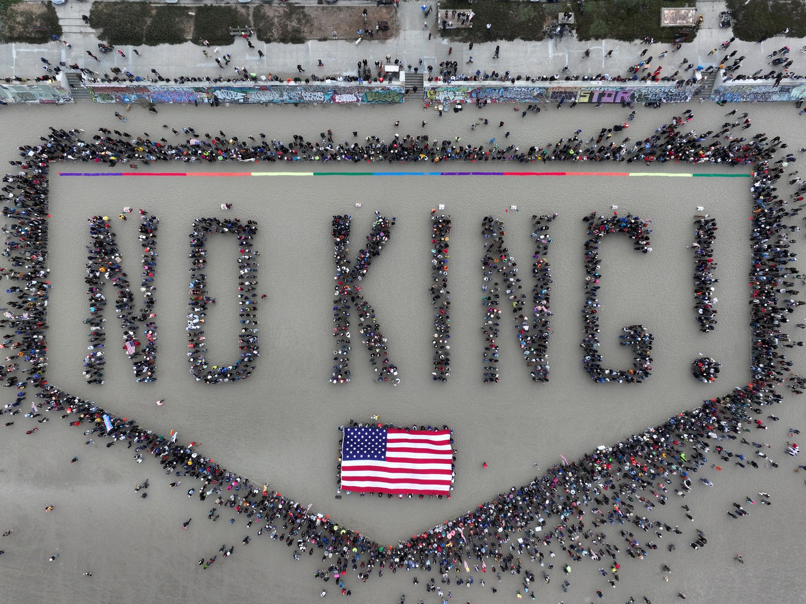 An aerial view of a crowd gathered on a beach, standing in groups, spelling out the words 