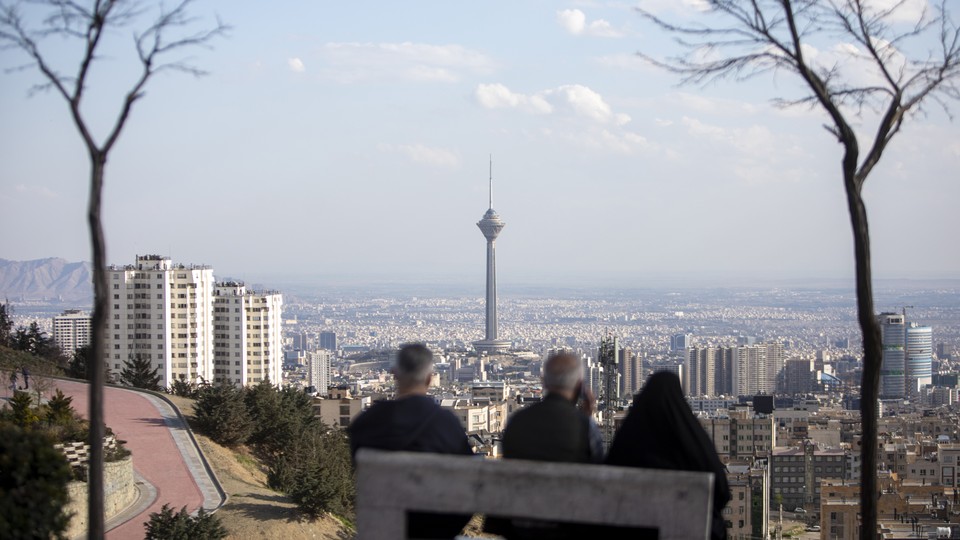 Photograph taken from behind of three figures on a bench overlooking Tehran's skyline.