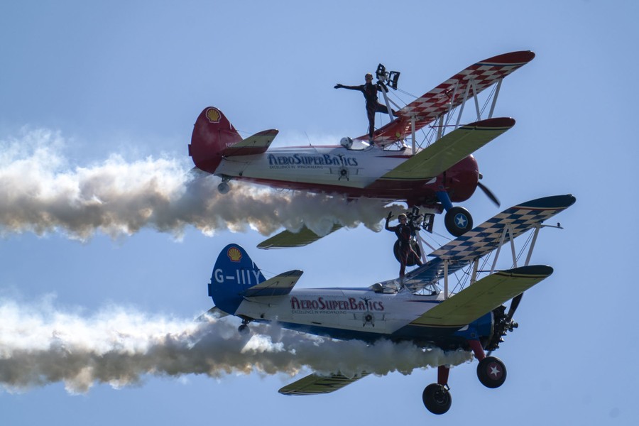 Wingwalkers stand on top of two biplanes that fly close together.