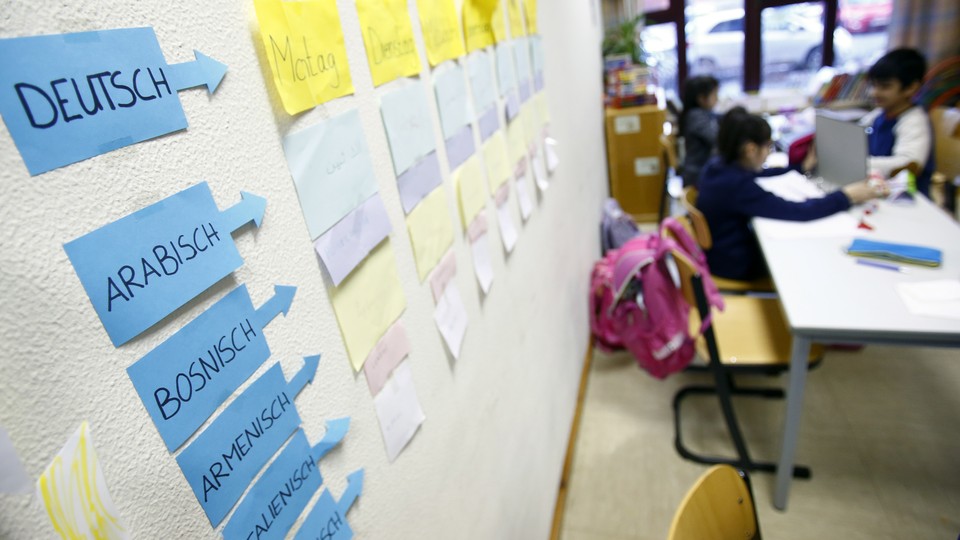 Students sit near a classroom wall with notes stuck to it naming languages and words in those languages.