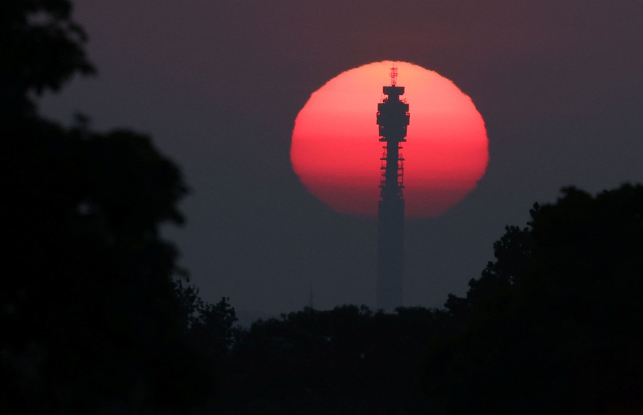 A sunrise is seen silhouetting a tall communication tower.