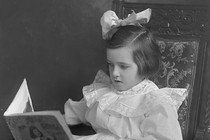 A photograph of a child reading a children's book while sitting in a large chair