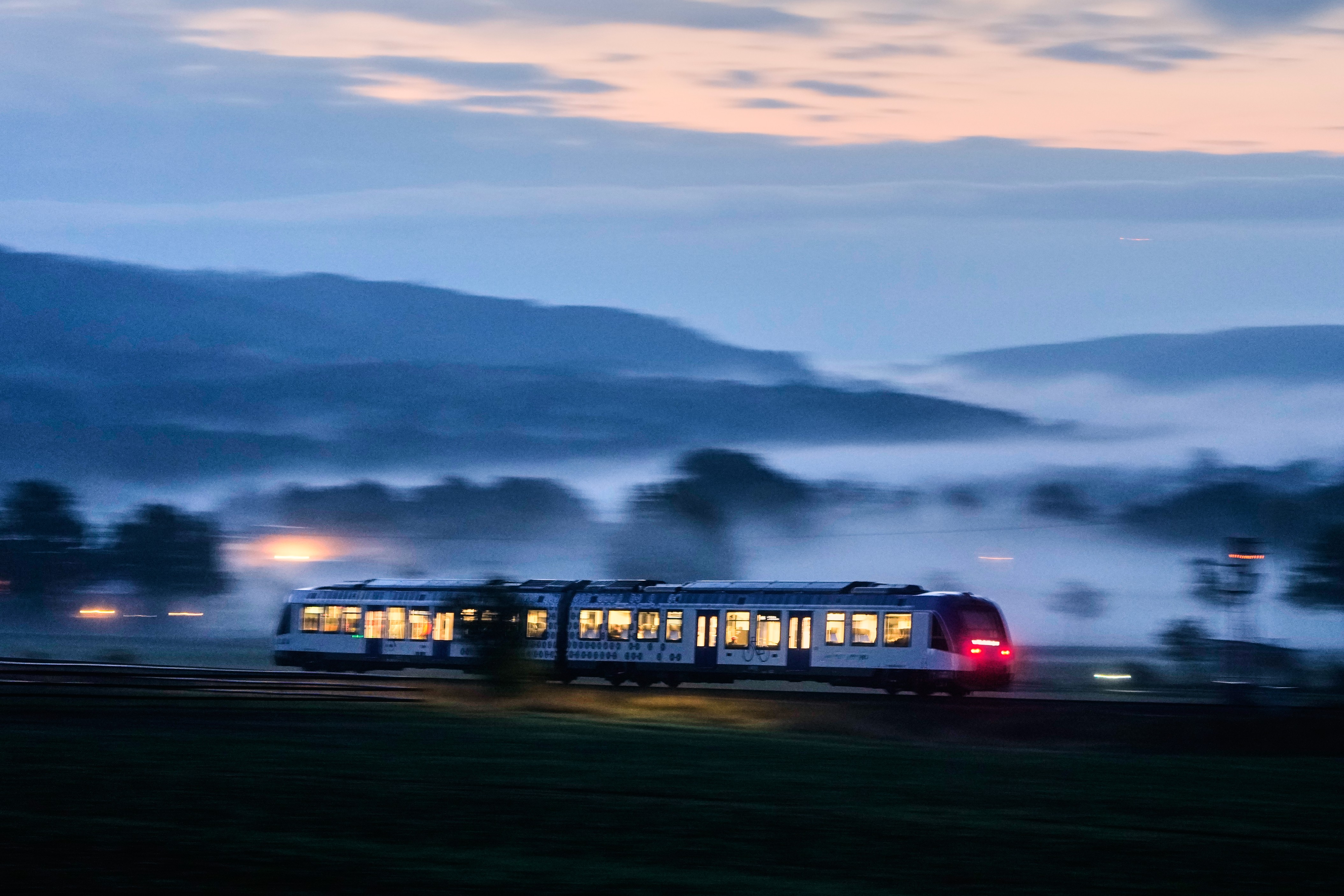 A small commuter train travels through a foggy landscape.