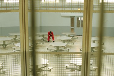 a color photographs of a man wearing a prison jumpsuit sitting alone in a lunch room