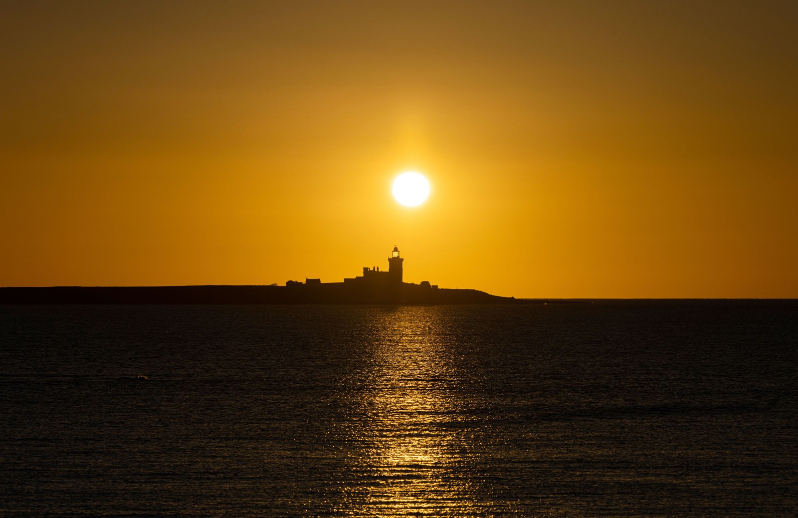 A sunrise, seen behind a distant lighthouse