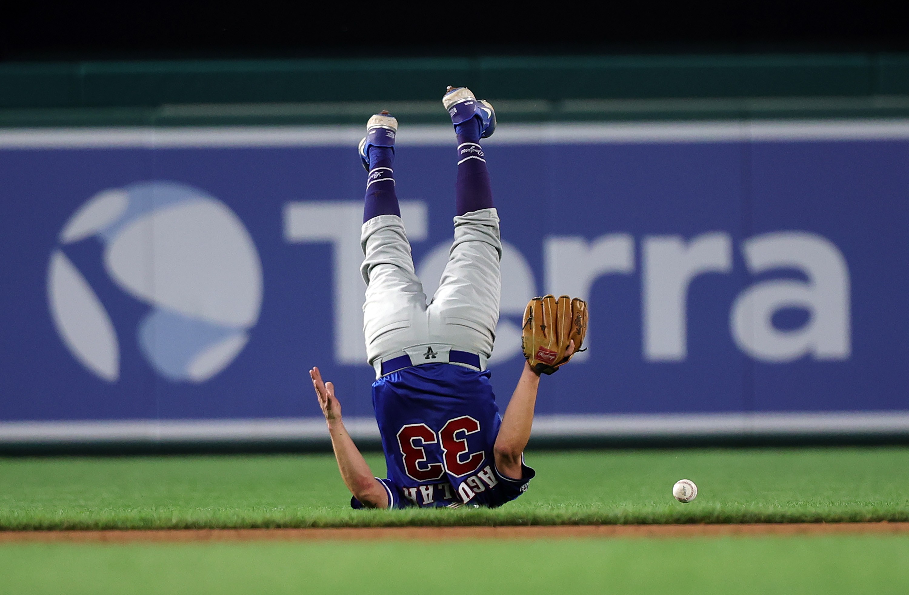 A person wearing a baseball uniform, upside down, tumbling after a ball