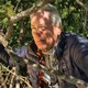 photo of Carl Hiaasen wearing blue jacket over gray fleece holding the branches of a mangrove