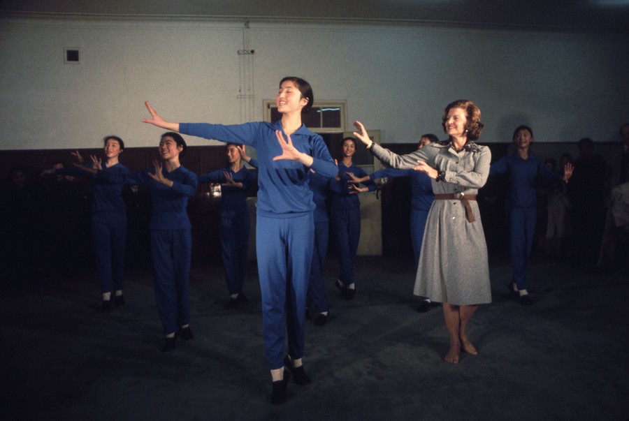 Betty Ford performs dance movements alongside 8 or 9 other dancers.