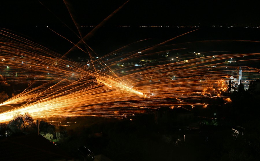 Firework rockets leave streaks of light in the sky above a small valley.