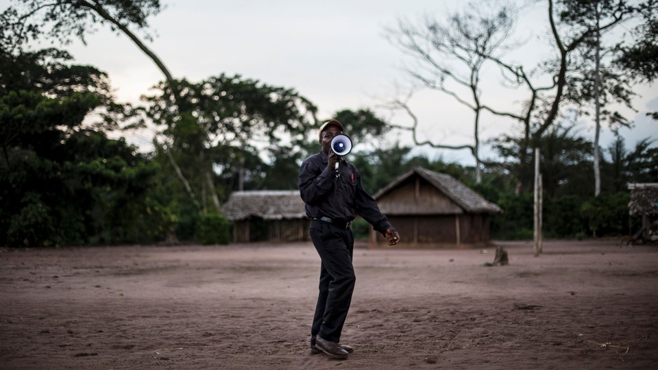 A health worker holds a megaphone to his mouth while standing on a patch of dirt.