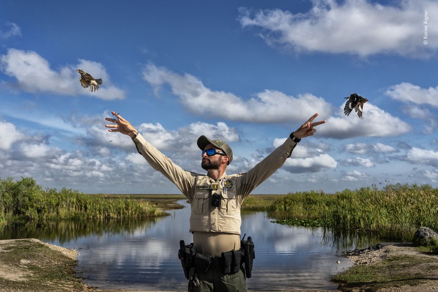 A person holds up both arms, releasing two small birds in the air.