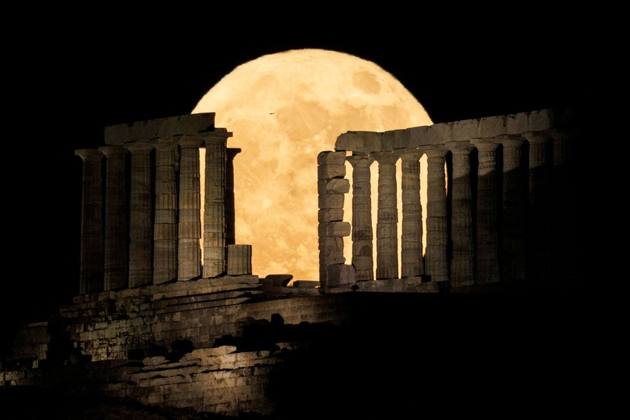 A full moon rises behind an ancient Greek temple.
