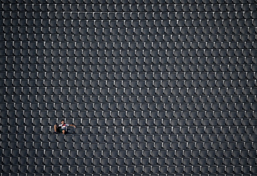 A soccer fan sits in stadium seating, alone among many rows of empty seats.