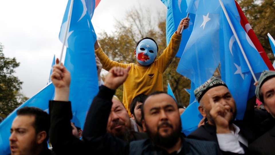 A boy in a blue mask raises two East Turkestan flags in a march.