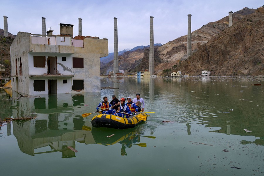 A half-dozen people in an inflatable raft paddle past flooded buildings.