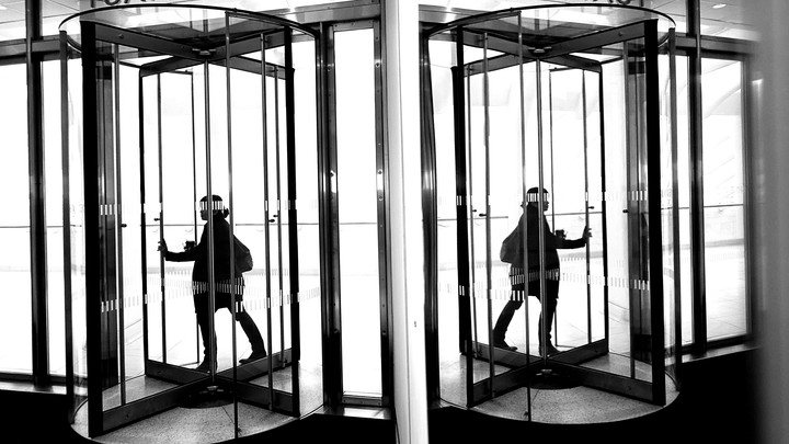 A woman walks through an office's revolving door next to a mirrored wall.