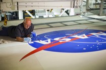 A person lies on a surface while painting a large NASA logo.