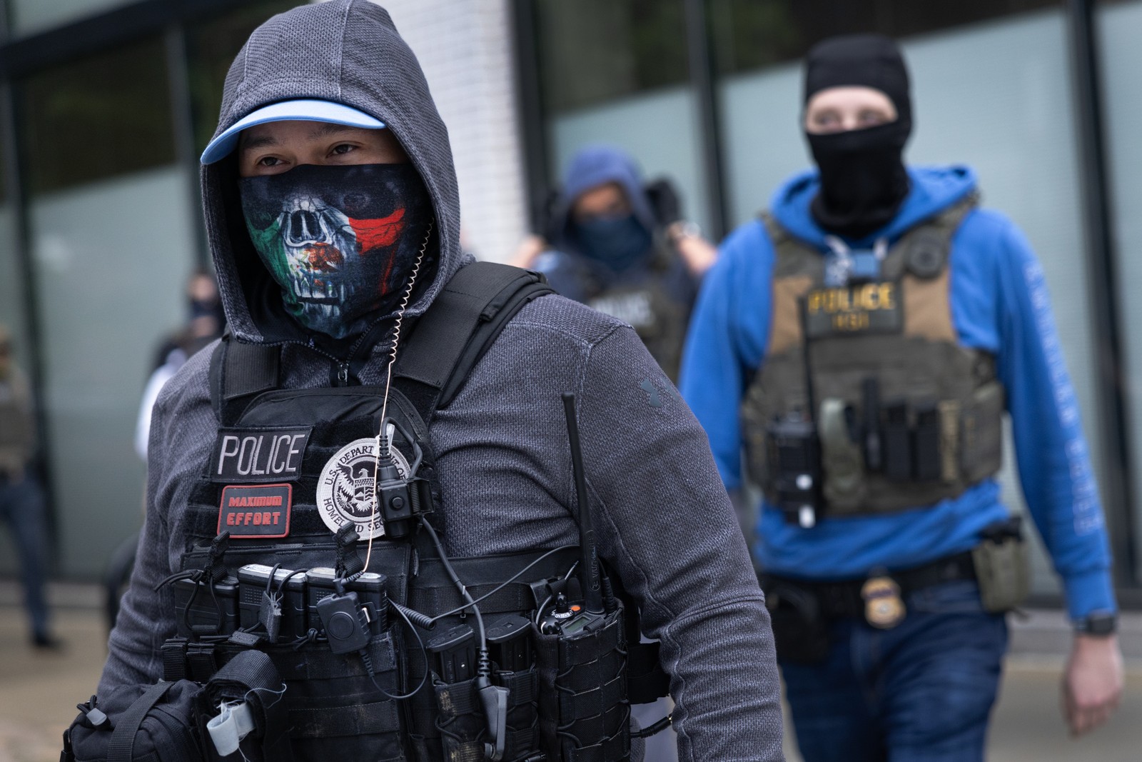 Two police officers, wearing a mix of official tactical gear and civilian hoodies and face coverings