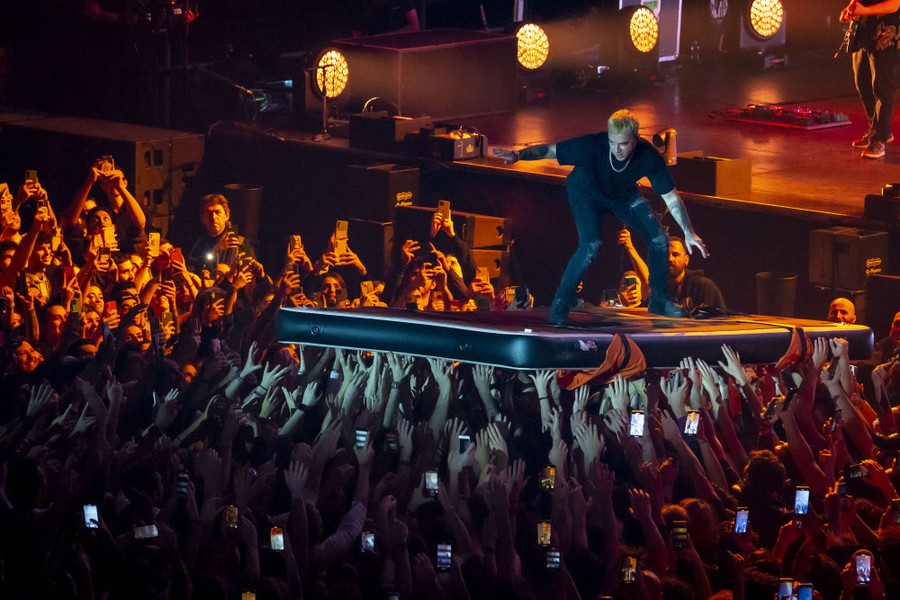 A performer stands on a soft mat that is held up by a crowd at a show.
