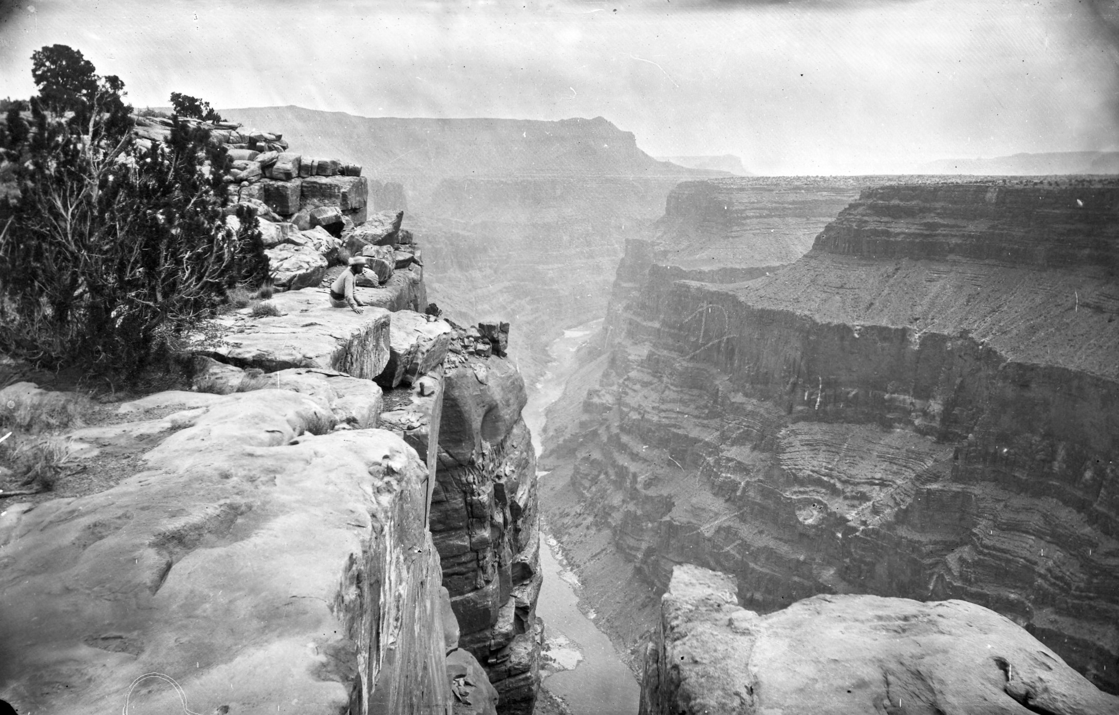A person sits near the edge of a cliff overlooking the Grand Canyon.
