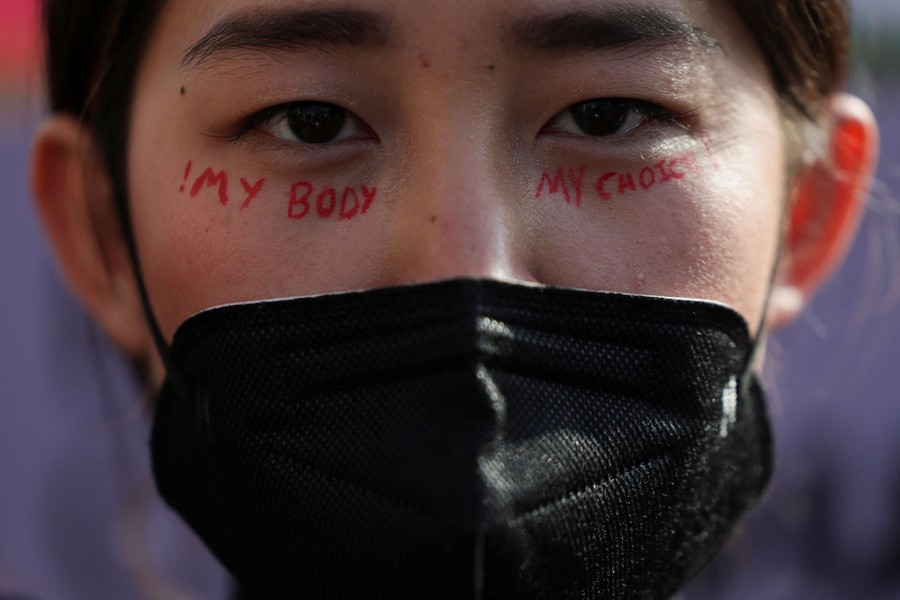 A woman wearing a face mask has the words "!My body My choice!" written on her face, below her eyes.