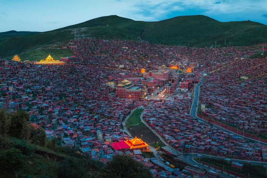 A night view of a dense settlement in a valley, surrounded by empty hills