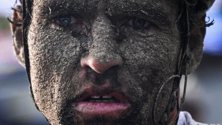 A close-up of a mud-covered cyclist staring into the distance
