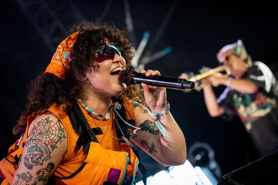 A performer sings into a microphone while a musician behind her plays a trumpet.